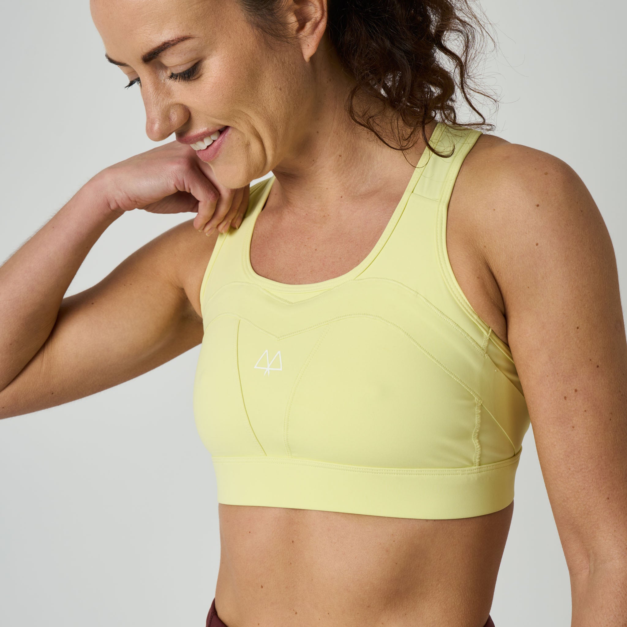 Woman wearing a yellow sports bra with a visible brand logo on a plain background