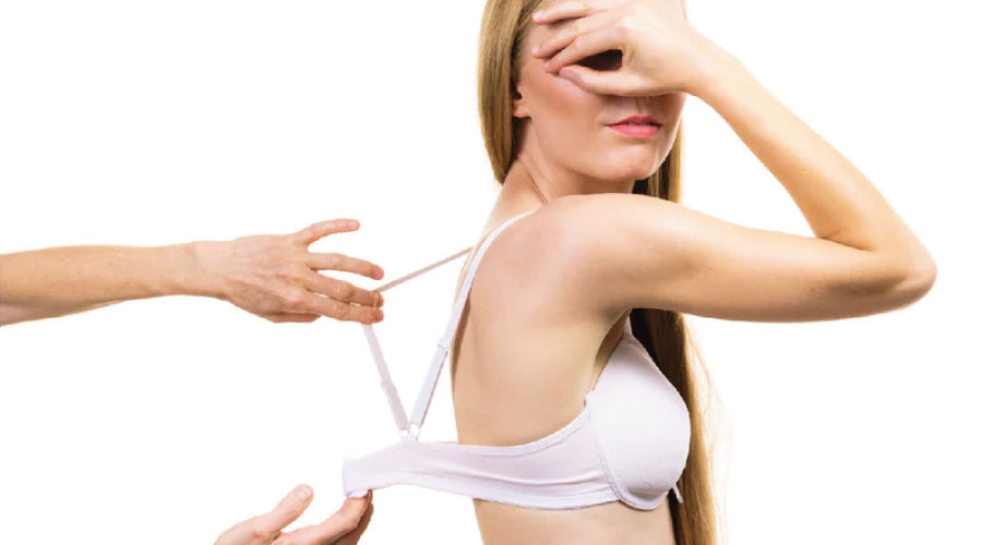 Young blonde haired girl looking awkward standing in a white t-shirt bra getting fitted by another person