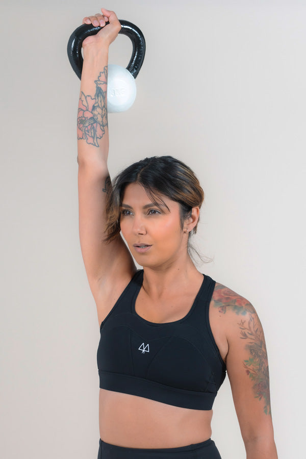 Woman lifts a kettlebell above her head while wearing a MAAREE Empower Sports Bra in Black