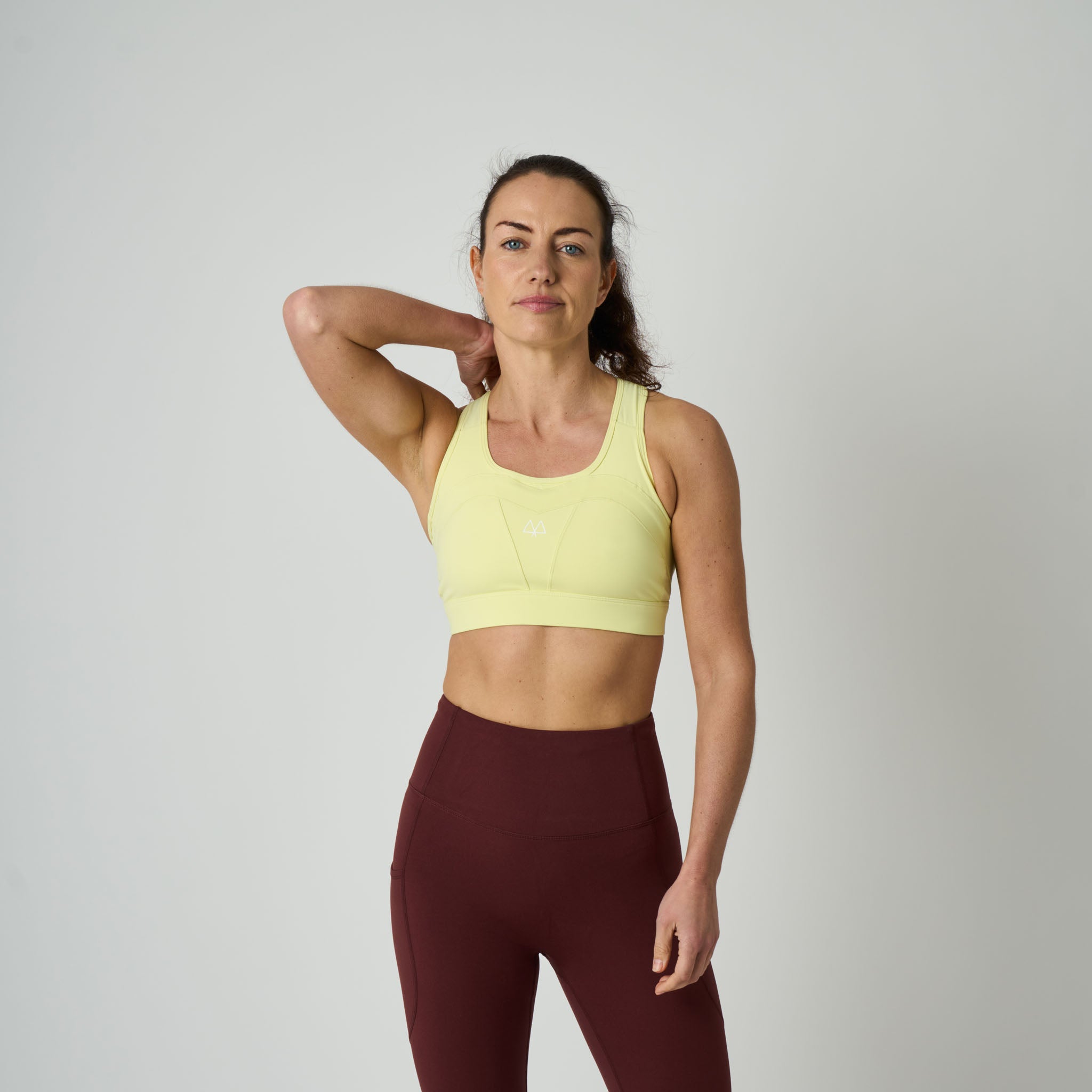 Woman wearing a yellow sports bra and maroon leggings on a plain background
