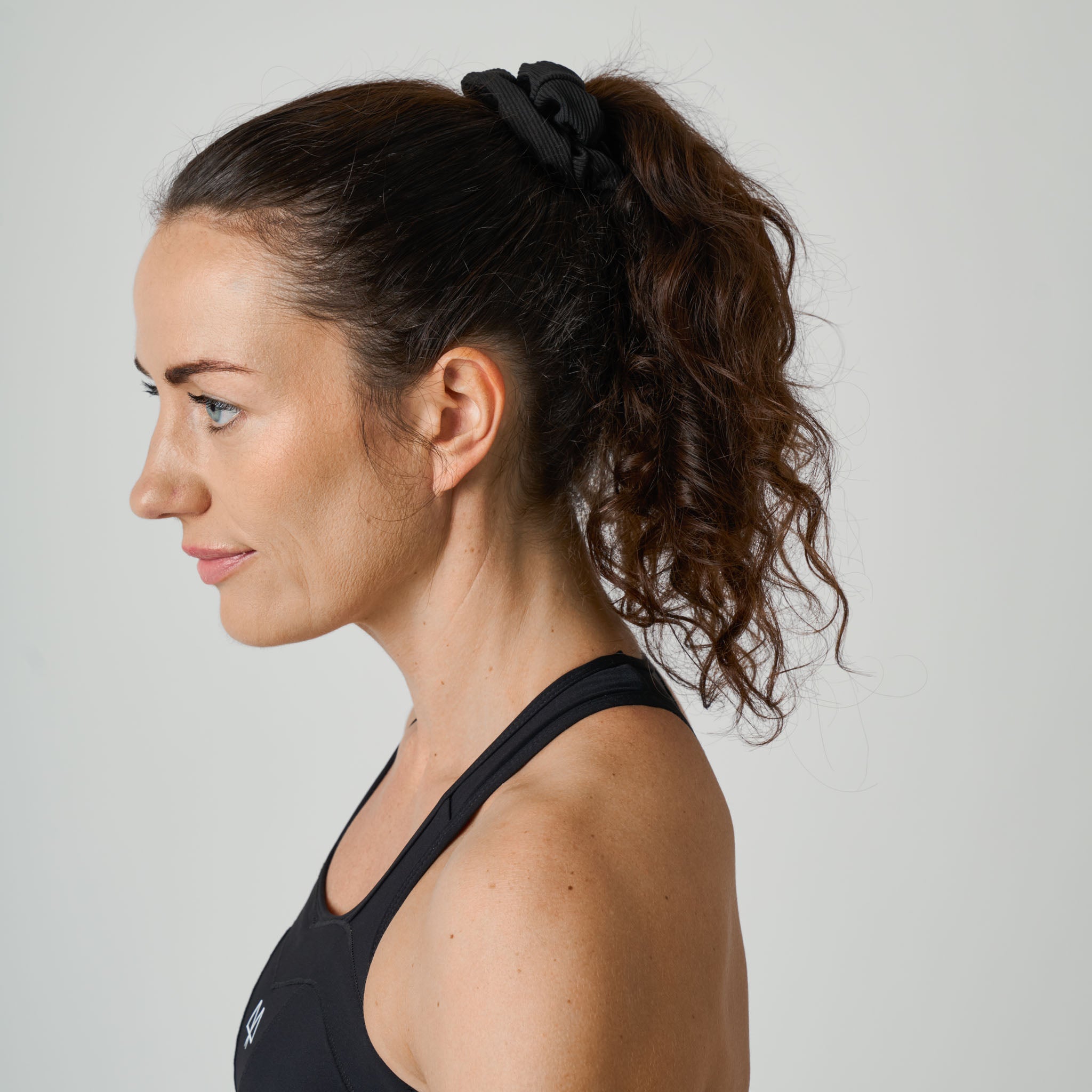 Woman with a ponytail wearing a black sports bra against a plain background