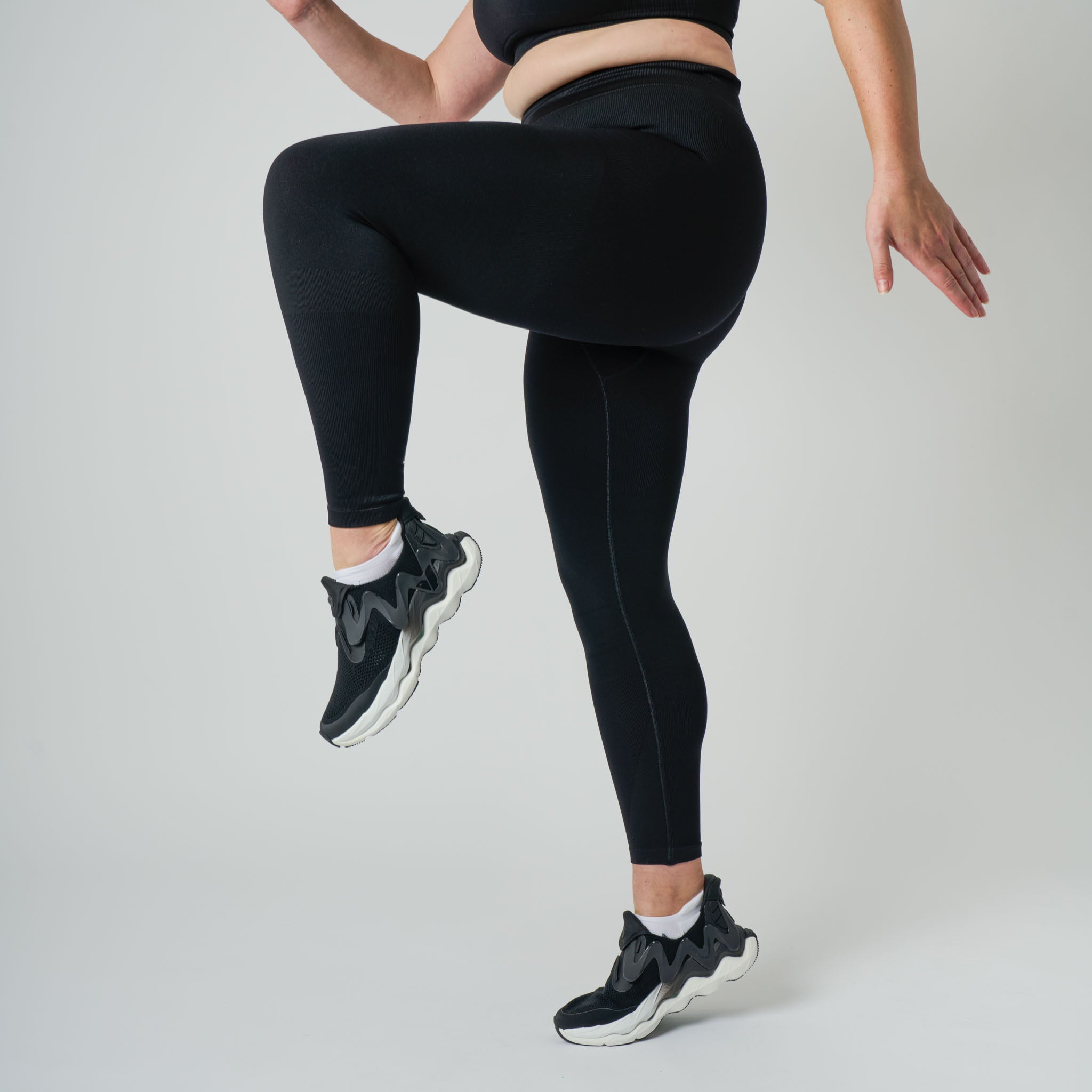 Person wearing black leggings and black athletic shoes on a light gray background