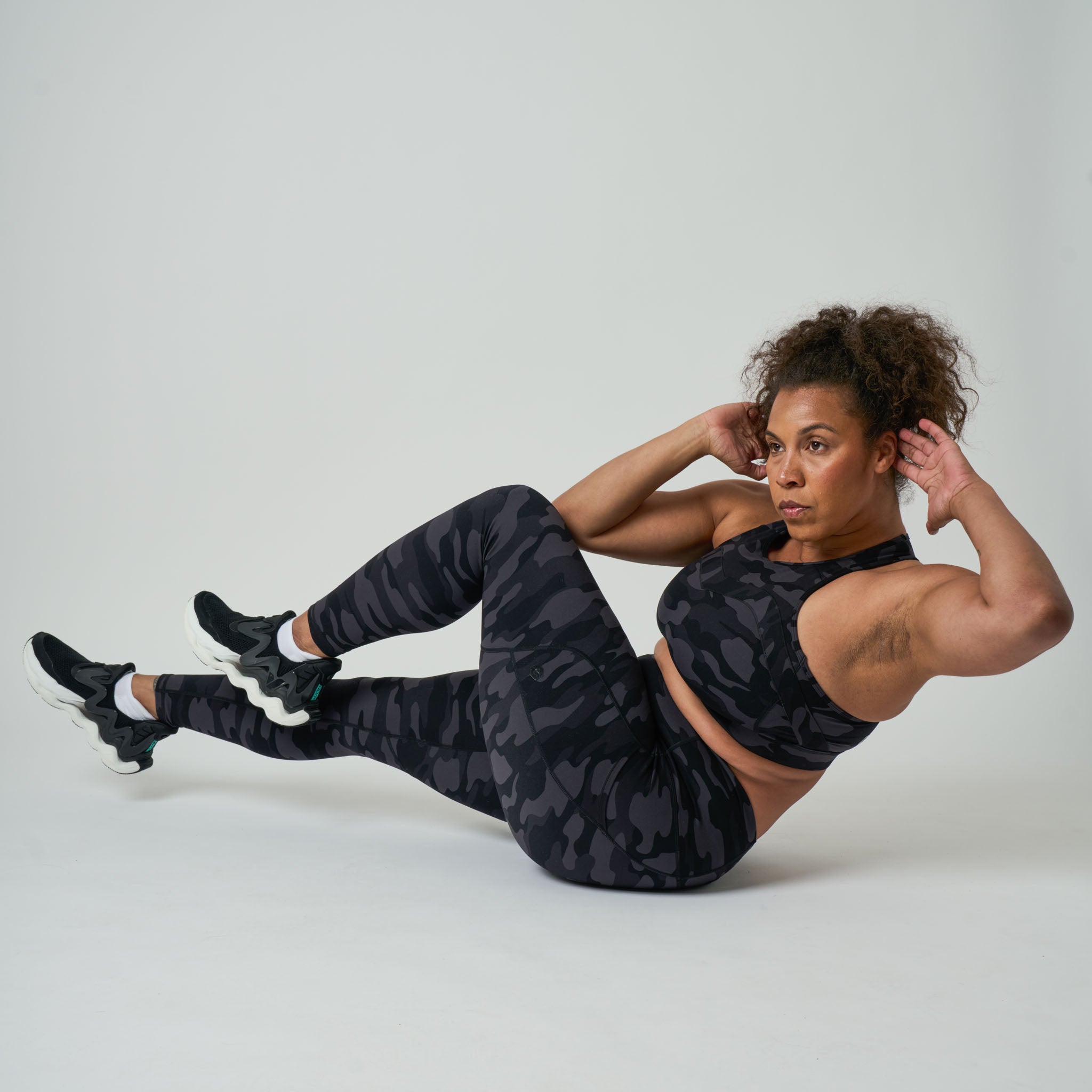 Woman in black athletic wear performing an exercise on a light gray background